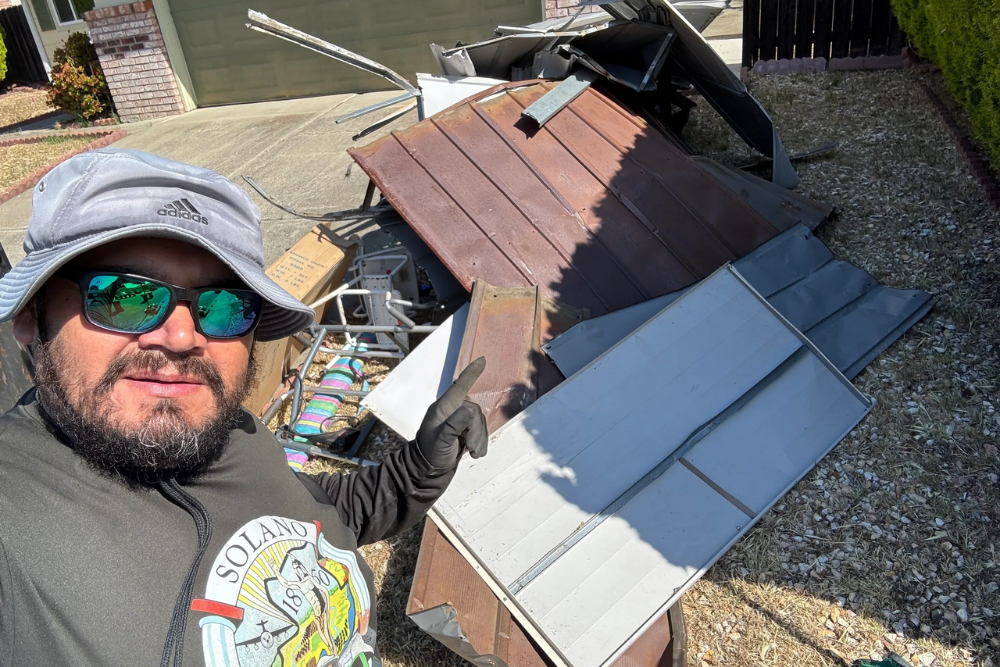 A No Limit Hauling technician pointing to a pile of dismantled metal shed panels during a backyard tear-down project in Fairfield, California.