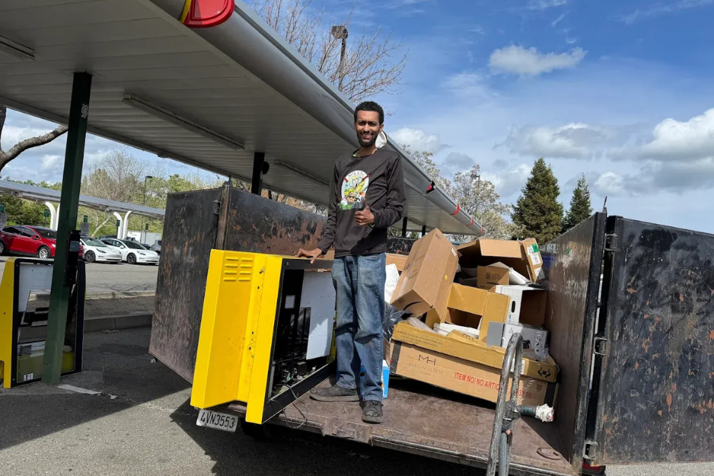 A junk removal professional loading commercial cardboard boxes and a large yellow electrical unit into a truck bed under a parking structure in Fairfield, California.