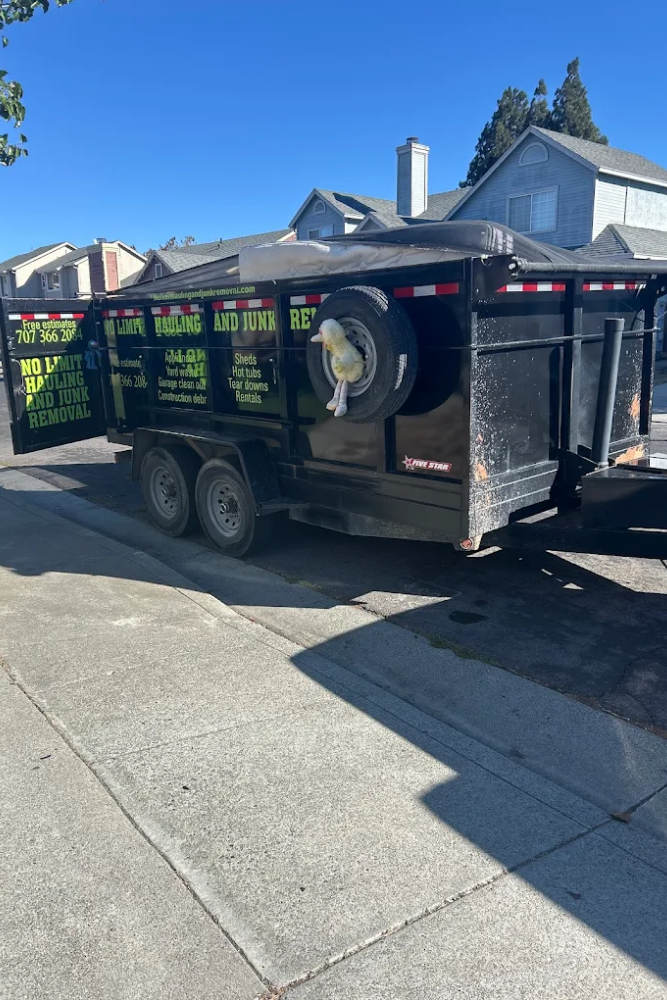 A black No Limit Hauling and Junk Removal utility trailer parked along a residential curb on a sunny day in Fairfield, California.